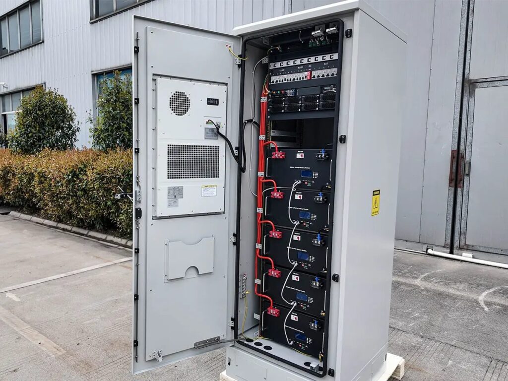 Open telecom battery cabinet with LiFePO4 battery modules and door-mounted cooling unit at an industrial site